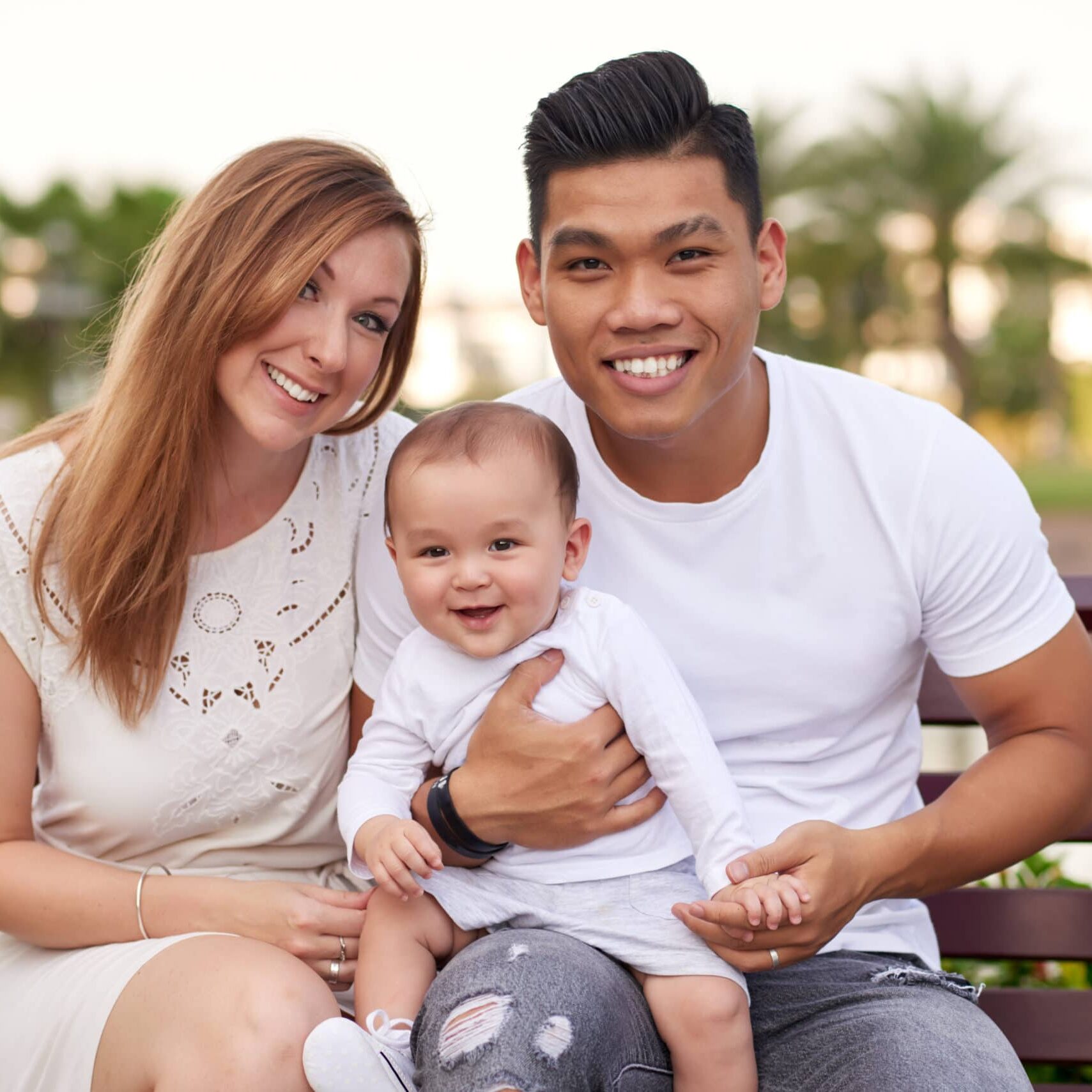 Cheerful smiling multi-ethnic family with baby boy sitting on bench